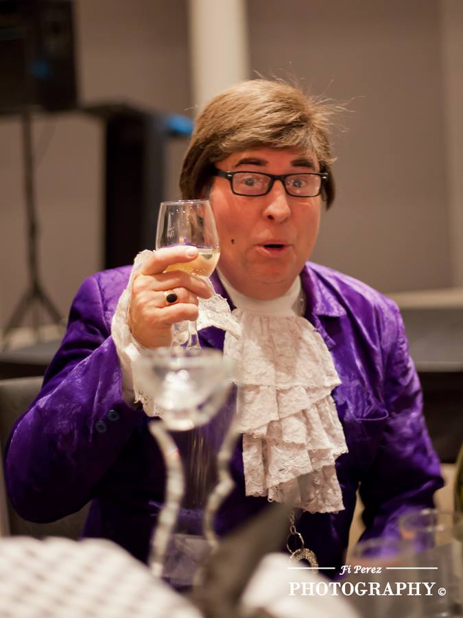 Austin Powers toasting with a glass of sparkling wine at a gala