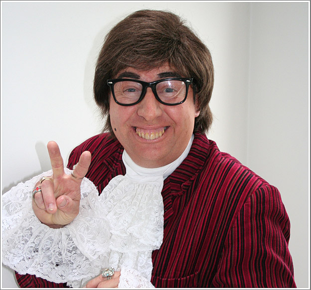 Close-up portrait of Gary Brown as Austin Powers in a striped jacket giving a peace sign