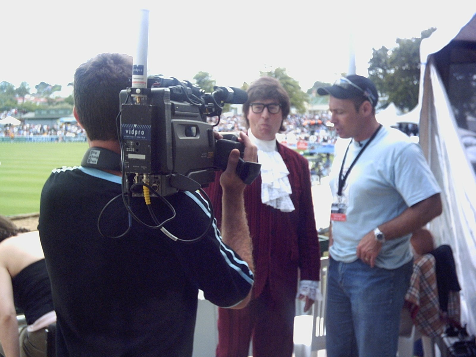 Austin Powers facing a broadcast camera crew at a cricket ground