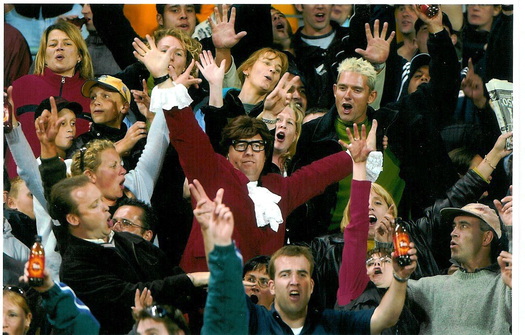 Austin Powers with arms raised in a packed stadium crowd