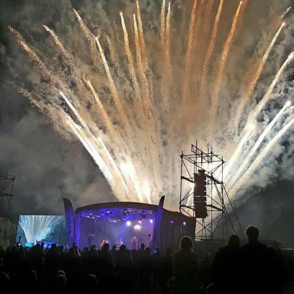 Fireworks erupting over an outdoor concert stage at night