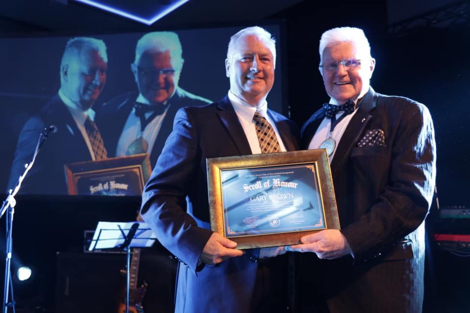 Gary Brown receiving a framed award on stage with three other men
