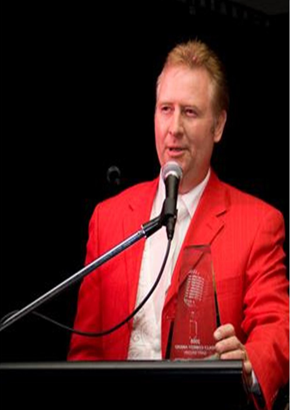 Gary Brown in a red jacket speaking at a lectern