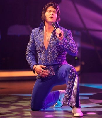 Elvis tribute artist in a purple sequin suit on a lit stage